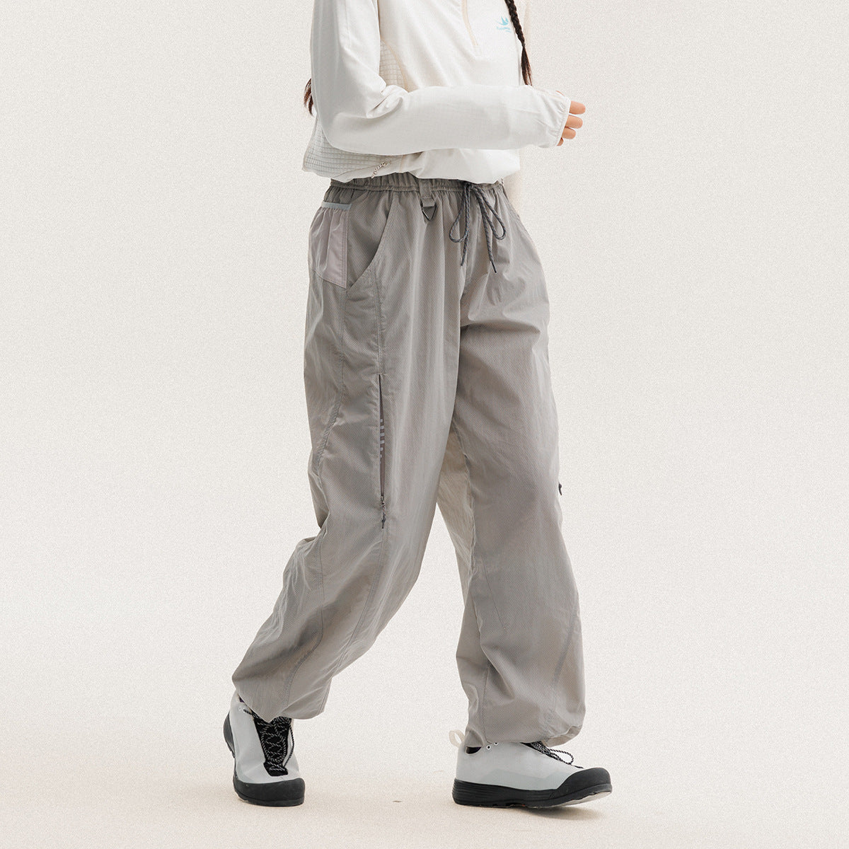 Model wearing loose light-gray drawstring pants with side pockets and a zip detail on one leg.