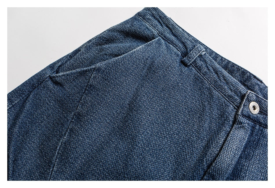 Close-up of dark blue denim trousers showing a curved pocket seam, waistband, belt loop and metal button.