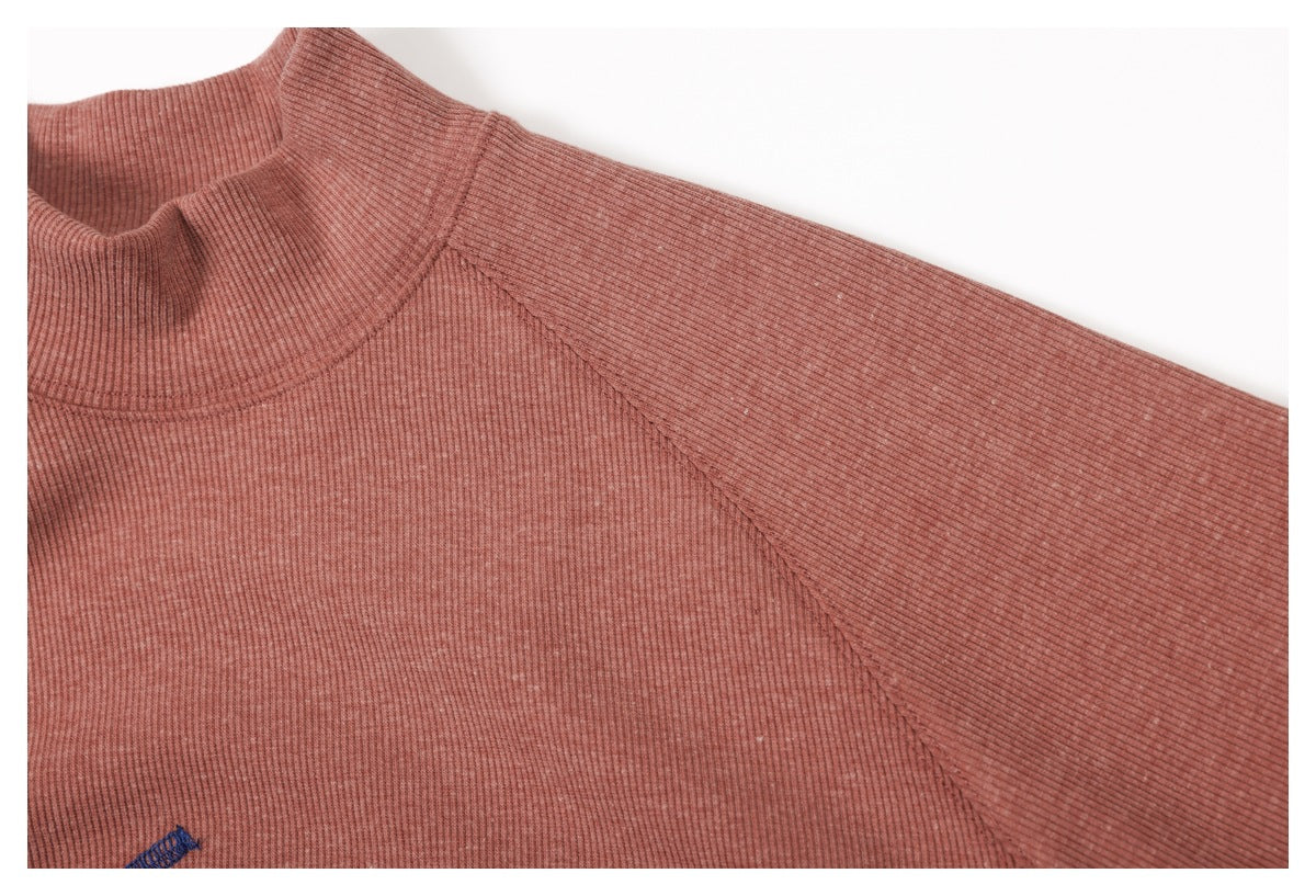 Close-up of a dusty rose ribbed mock-neck sweater, showing the shoulder seam and partial blue embroidery.
