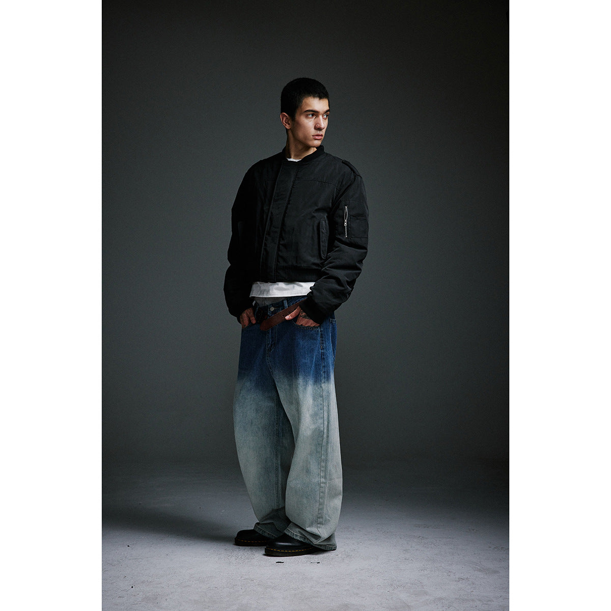 Full-length model in a black bomber jacket, very wide blue-to-pale washed jeans, brown belt and black shoes.