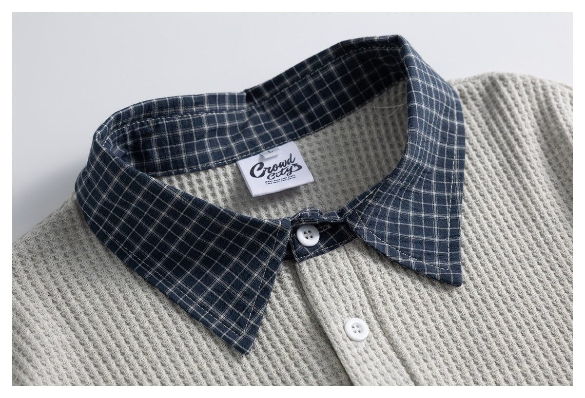 Close-up of a light gray textured polo with a navy plaid collar and white buttons.