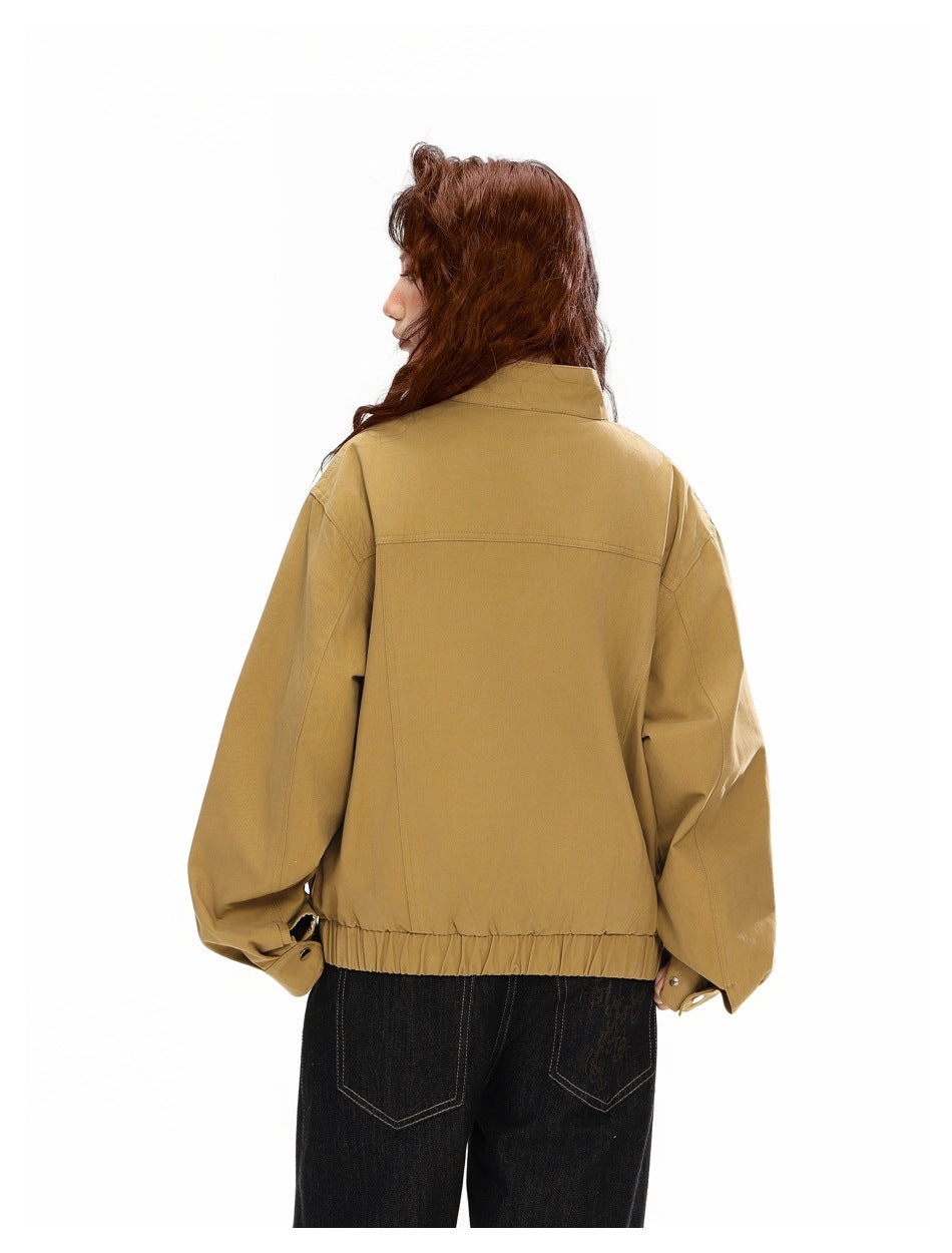 Close rear view of a model wearing an ochre tan jacket with a horizontal back yoke and elastic hem.