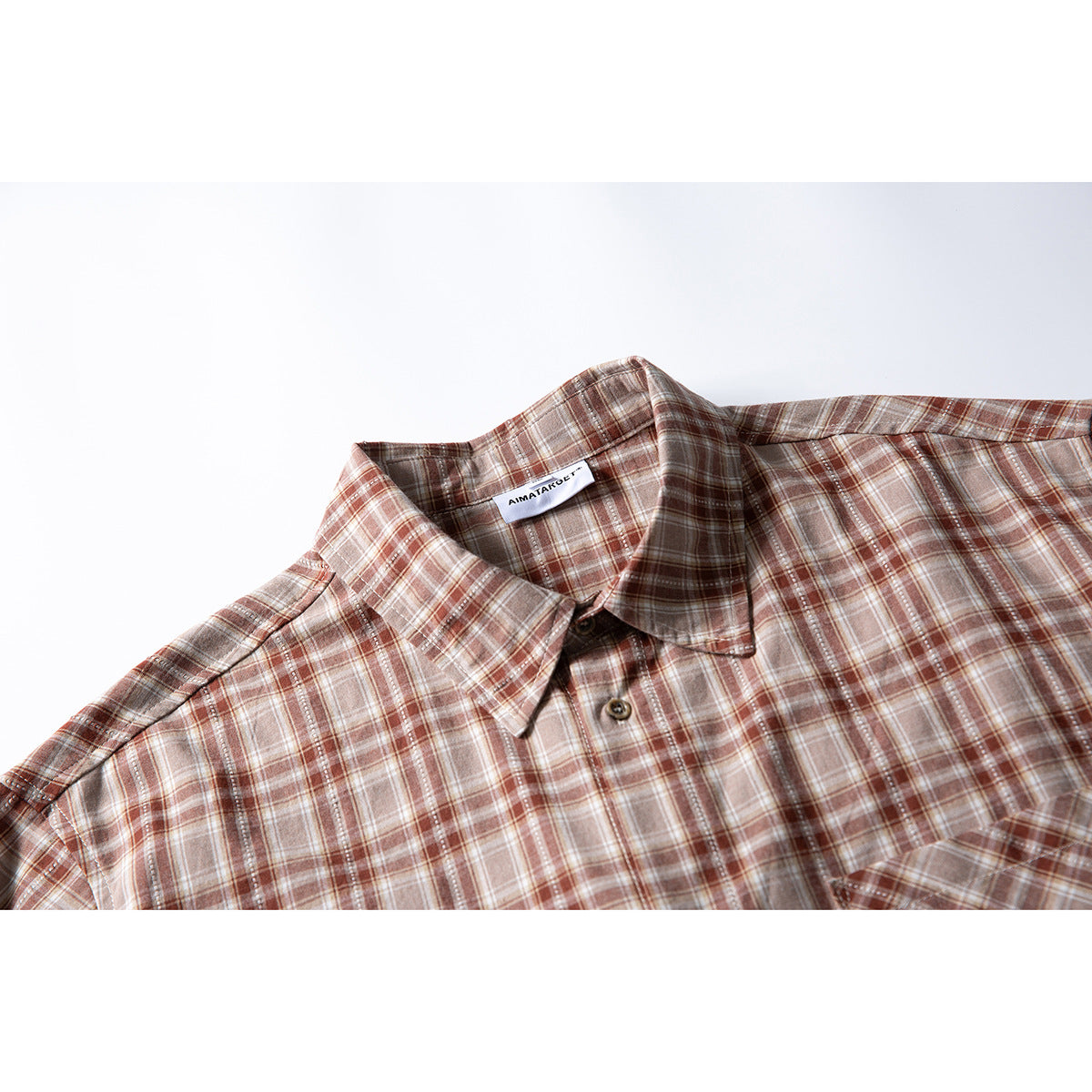 Close view of a brown, cream, and rust plaid button-up shirt with a pointed collar and front buttons.