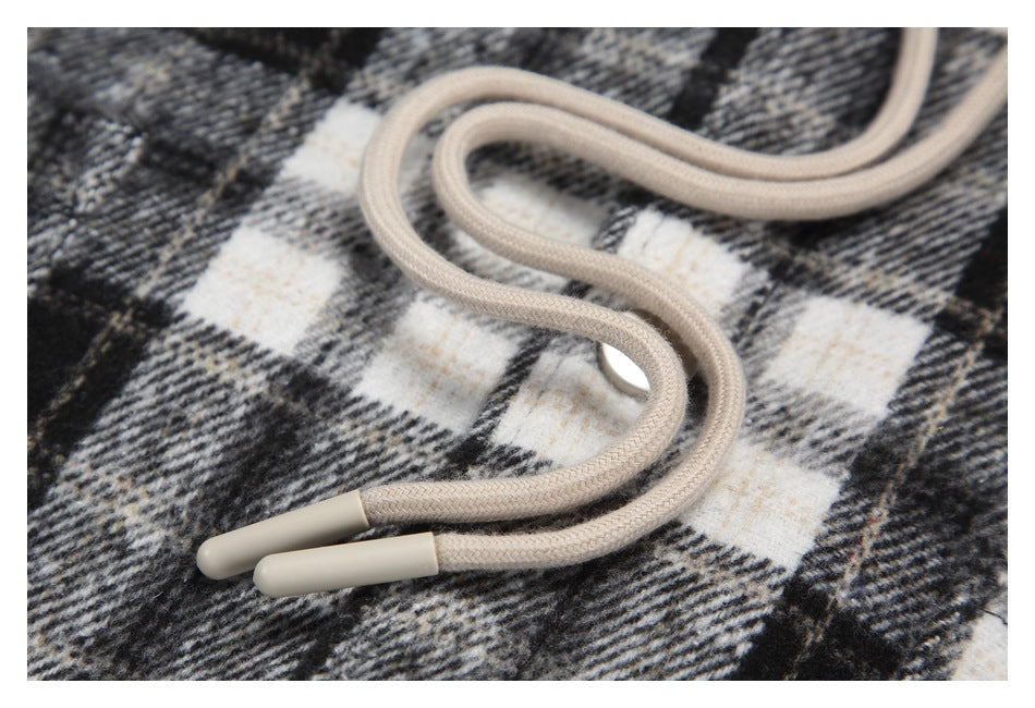 Close-up of cream hood drawstrings with molded tips against black, gray, and cream plaid fabric.