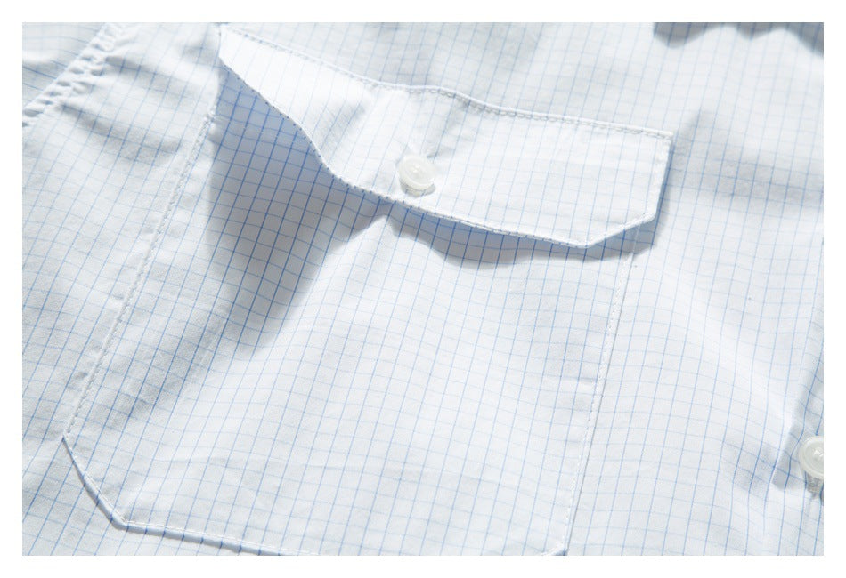 Close-up of a white shirt with a light blue grid pattern, showing a buttoned chest pocket flap.
