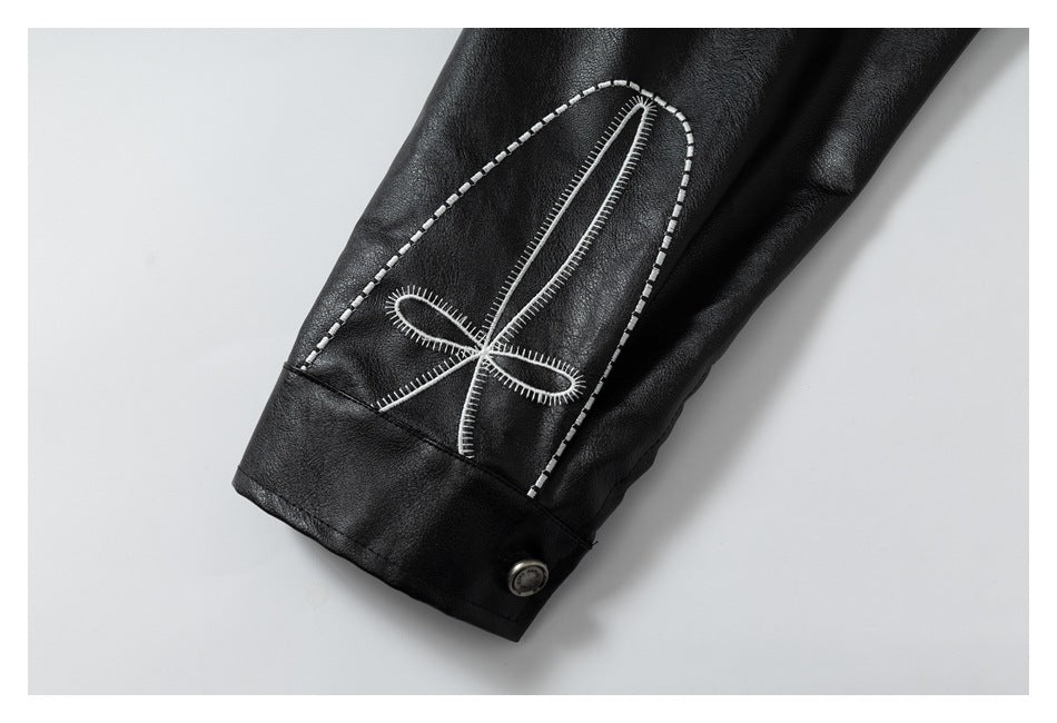 Close-up of a black jacket cuff with a large white embroidered loop motif and button.
