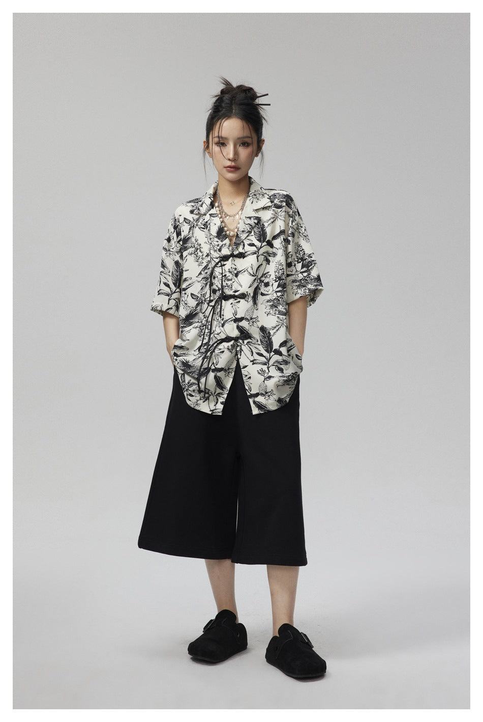 Model wearing the black and cream botanical print short-sleeve shirt with black wide-leg cropped pants and black clogs