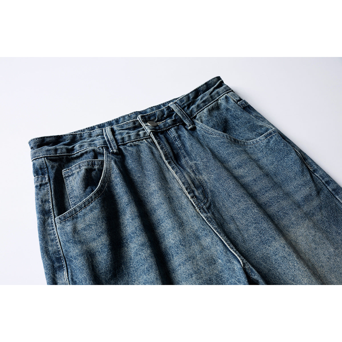 Close-up of blue washed jeans from the front, showing the waistband, button, fly, belt loops and pockets.