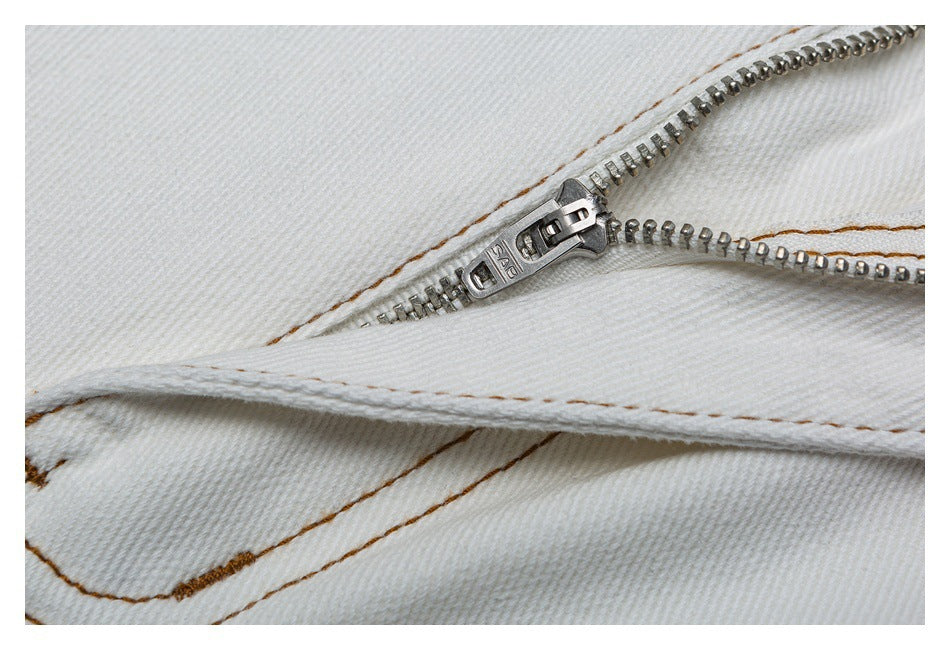 Close-up of a metal zipper on white denim with brown contrast stitching.