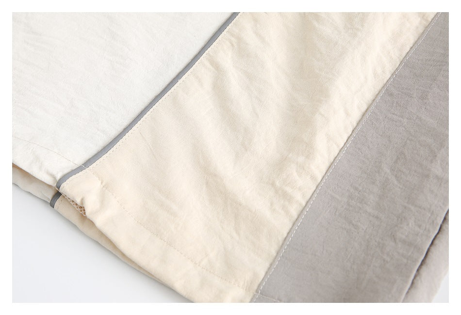 Close-up of a folded cream, white, and gray top showing panel seams and gray trim.