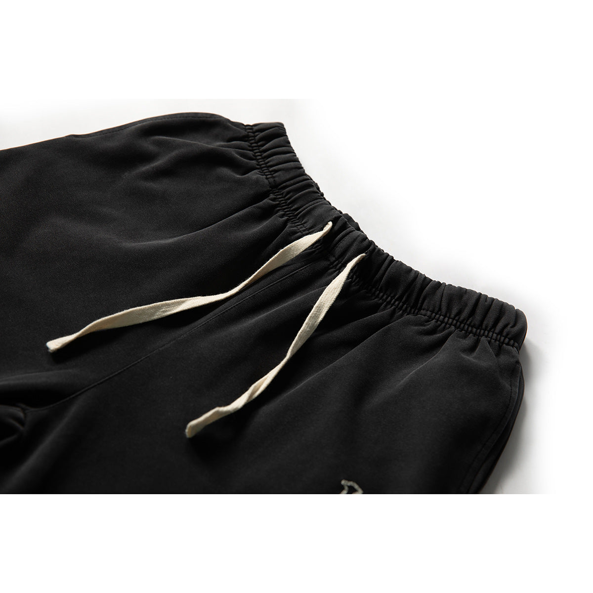 Close-up of black joggers showing the gathered elastic waistband and two cream drawstrings.