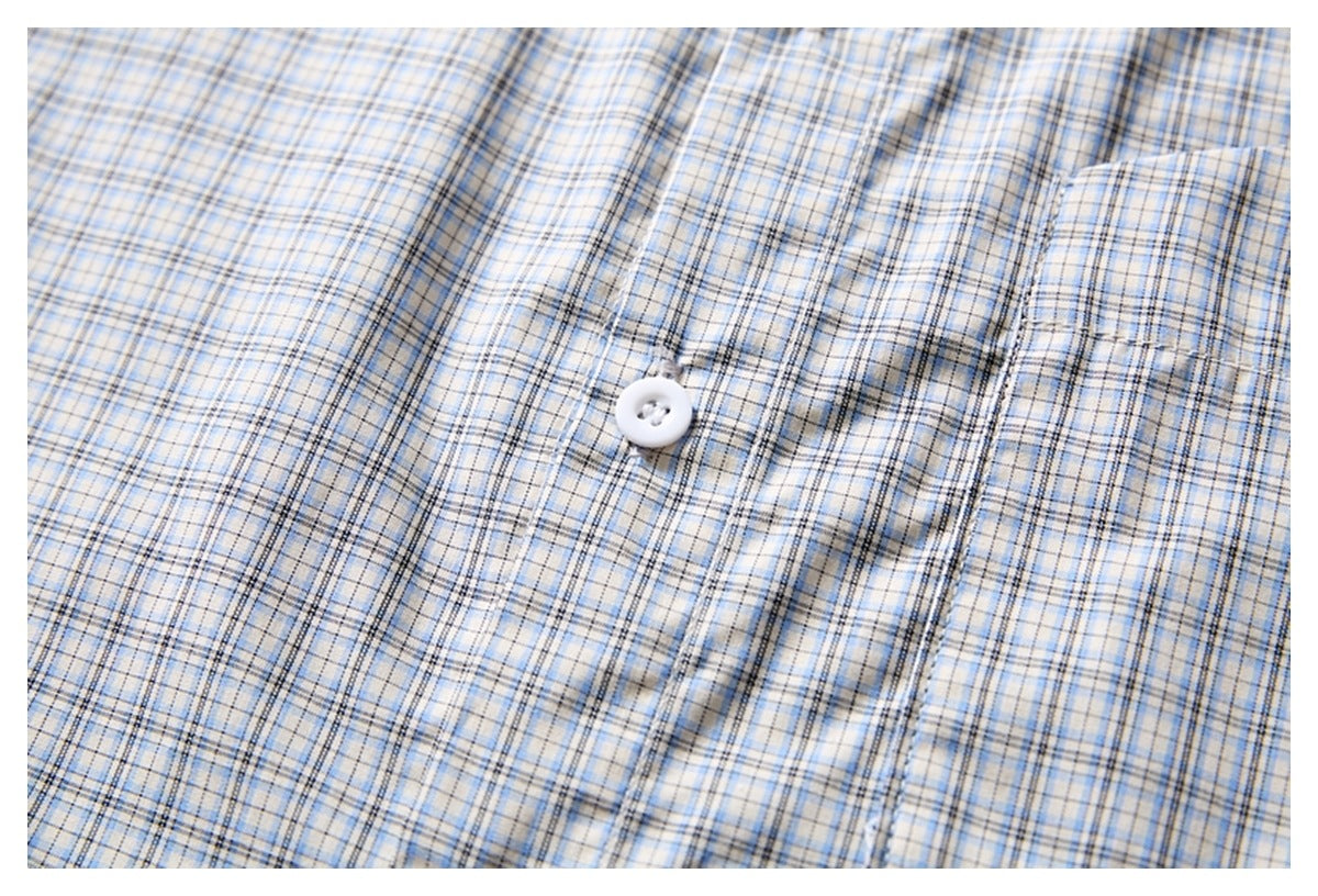 Close-up of a white shirt with a blue and gray plaid pattern, showing a white button and pocket seam.