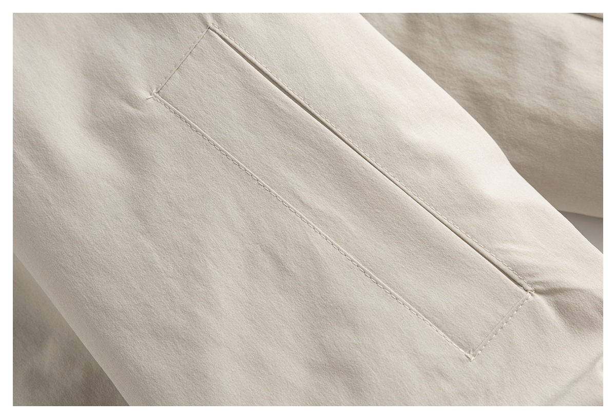 Close-up of a stitched rectangular pocket on a light beige garment.