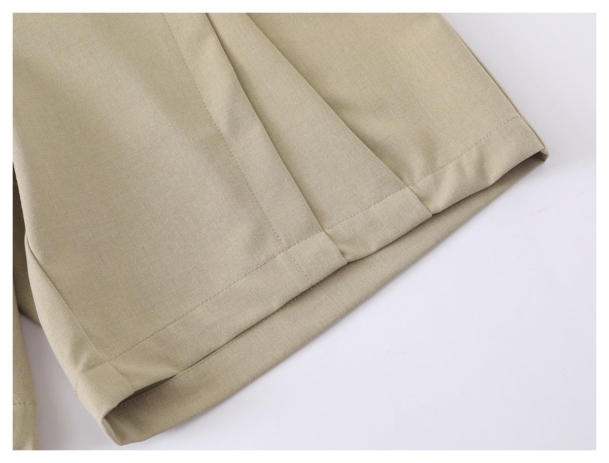 Close-up of the wide folded hem and stitched seams on beige trouser legs.