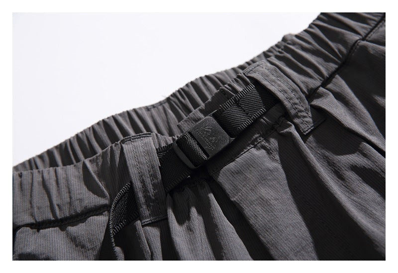Close-up of the black buckle belt and gathered elastic waistband on the charcoal shorts.