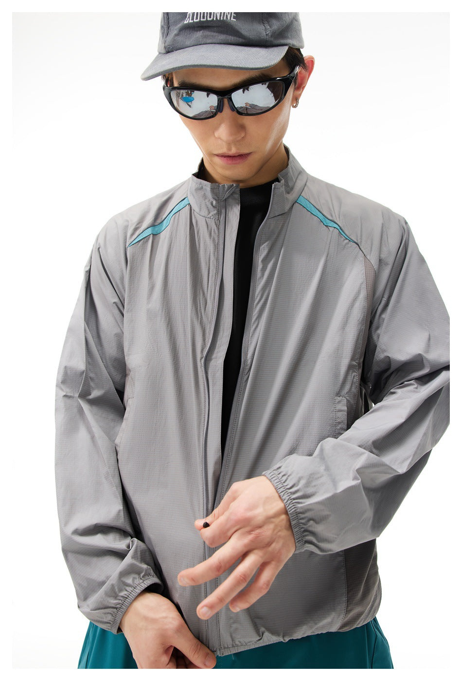 Close view of a model wearing a gray zip-up jacket with turquoise shoulder accents and a dark cap.