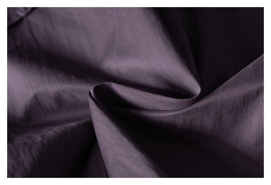 Close-up of mauve-gray pants fabric draped into folds, showing its smooth surface and subtle sheen.