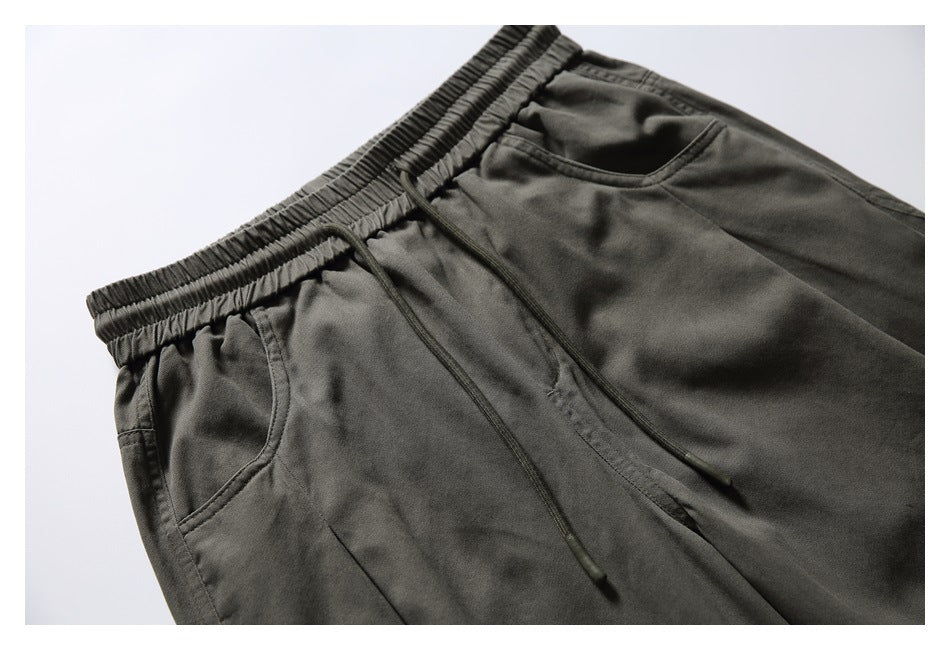 Close-up of dark olive pants showing the gathered elastic waistband, drawstrings, and front pockets.