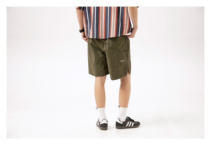 Rear view of a model wearing olive-green knee-length shorts with a rear pocket and side slit.