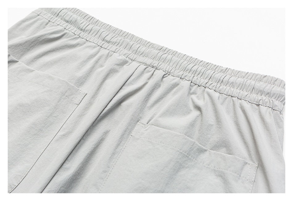 Close-up of light gray shorts showing the elastic waistband, seams, and large patch pockets.