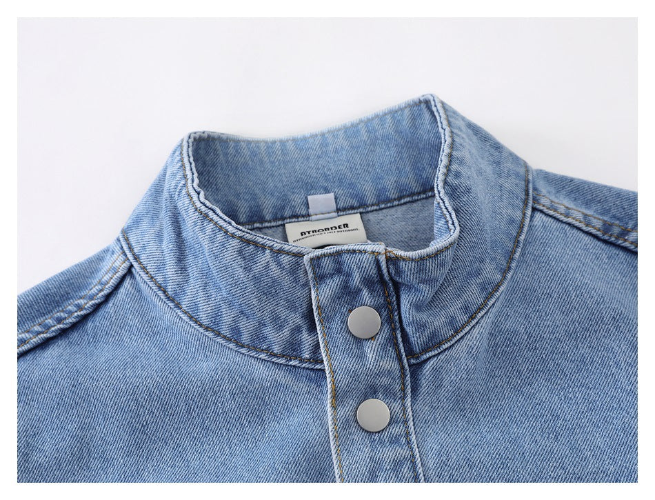 Close-up of a light blue denim jacket collar, neck label, and silver snap-button placket.