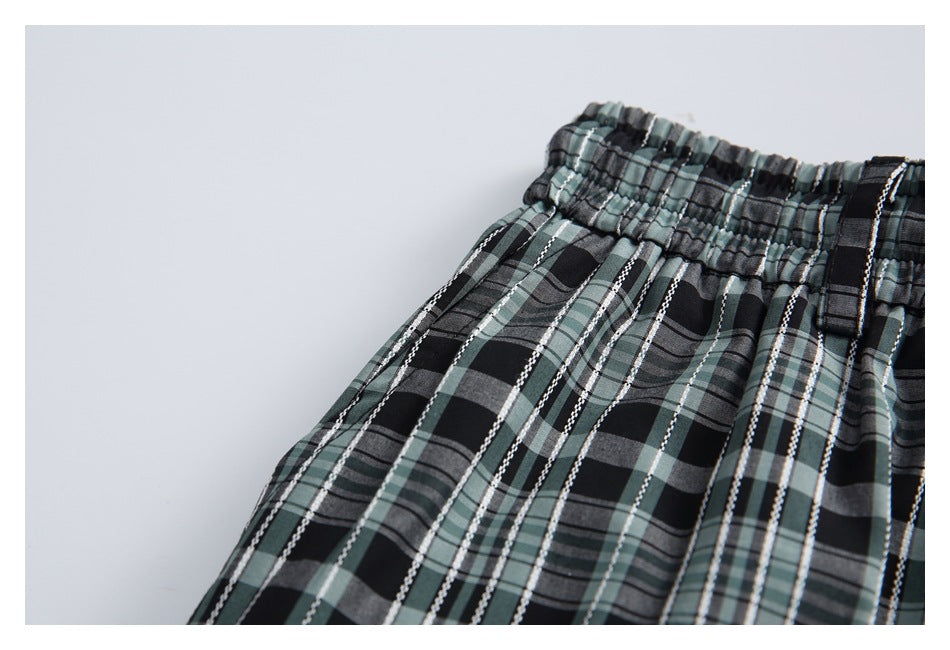 Close-up of the elastic waist and belt loop on black, gray, and muted green plaid trousers.