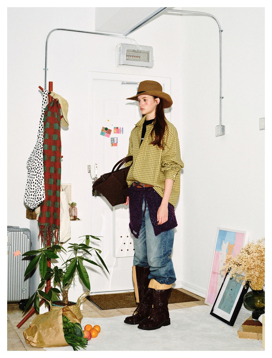 Side view of a model wearing an olive-yellow plaid shirt, brown hat, jeans, and tall brown boots.