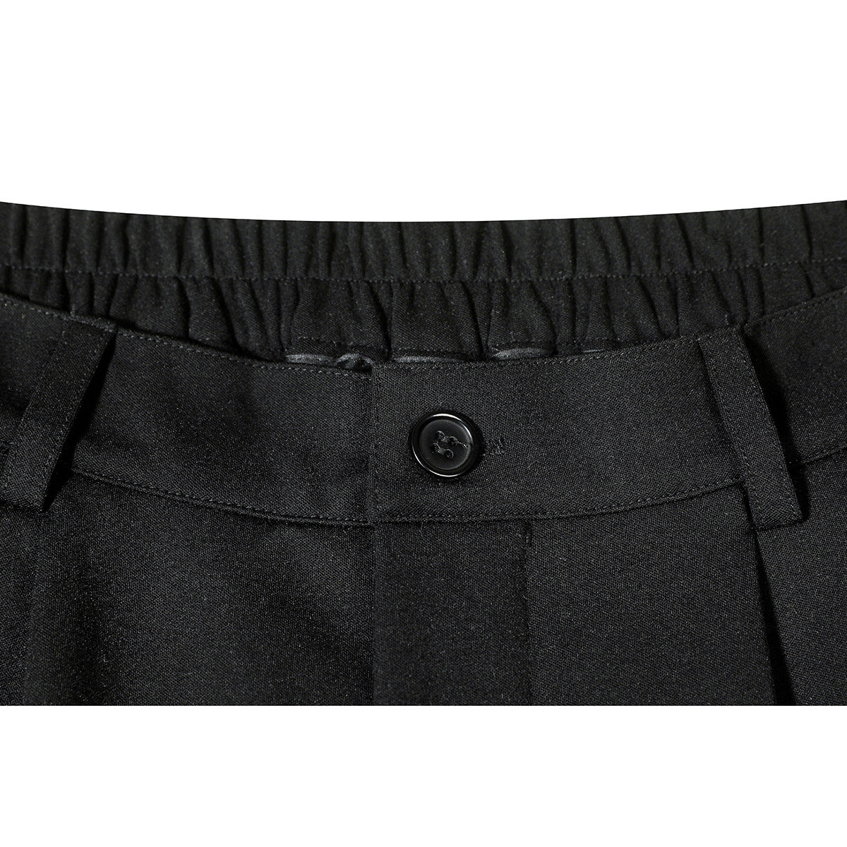 Close-up of black trousers showing a gathered waistband, buttoned tab, belt loops and front pleats.