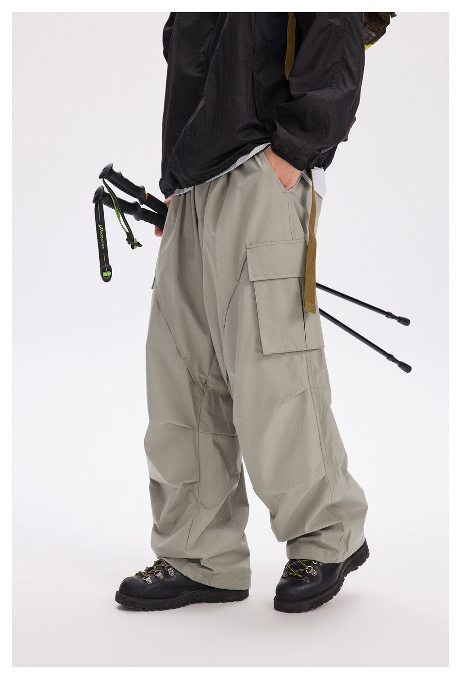 Side view of a model wearing loose light gray cargo pants with a large flap pocket and angular panel seams.