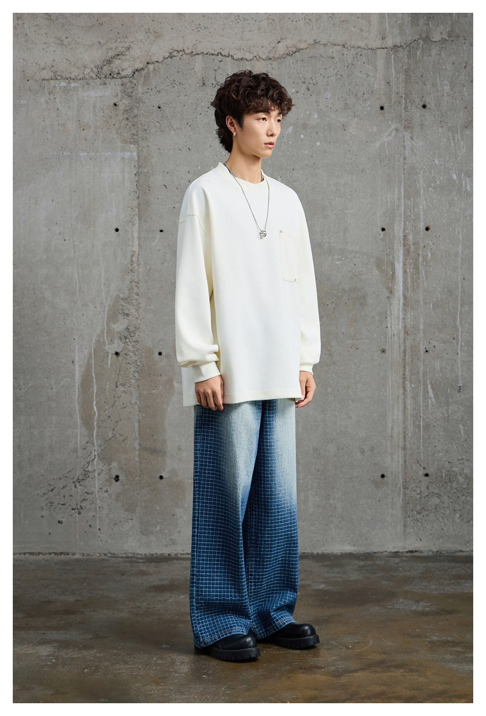 Model wearing an oversized ivory crewneck sweatshirt with a chest pocket and blue checkered wide-leg trousers.