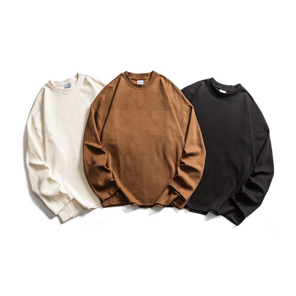 Three plain long-sleeve crewneck tops arranged flat in ivory, camel brown, and black.