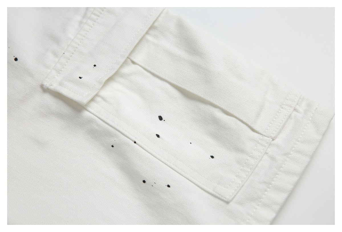 Close-up of off-white garment seams and hem with scattered black paint-like marks.