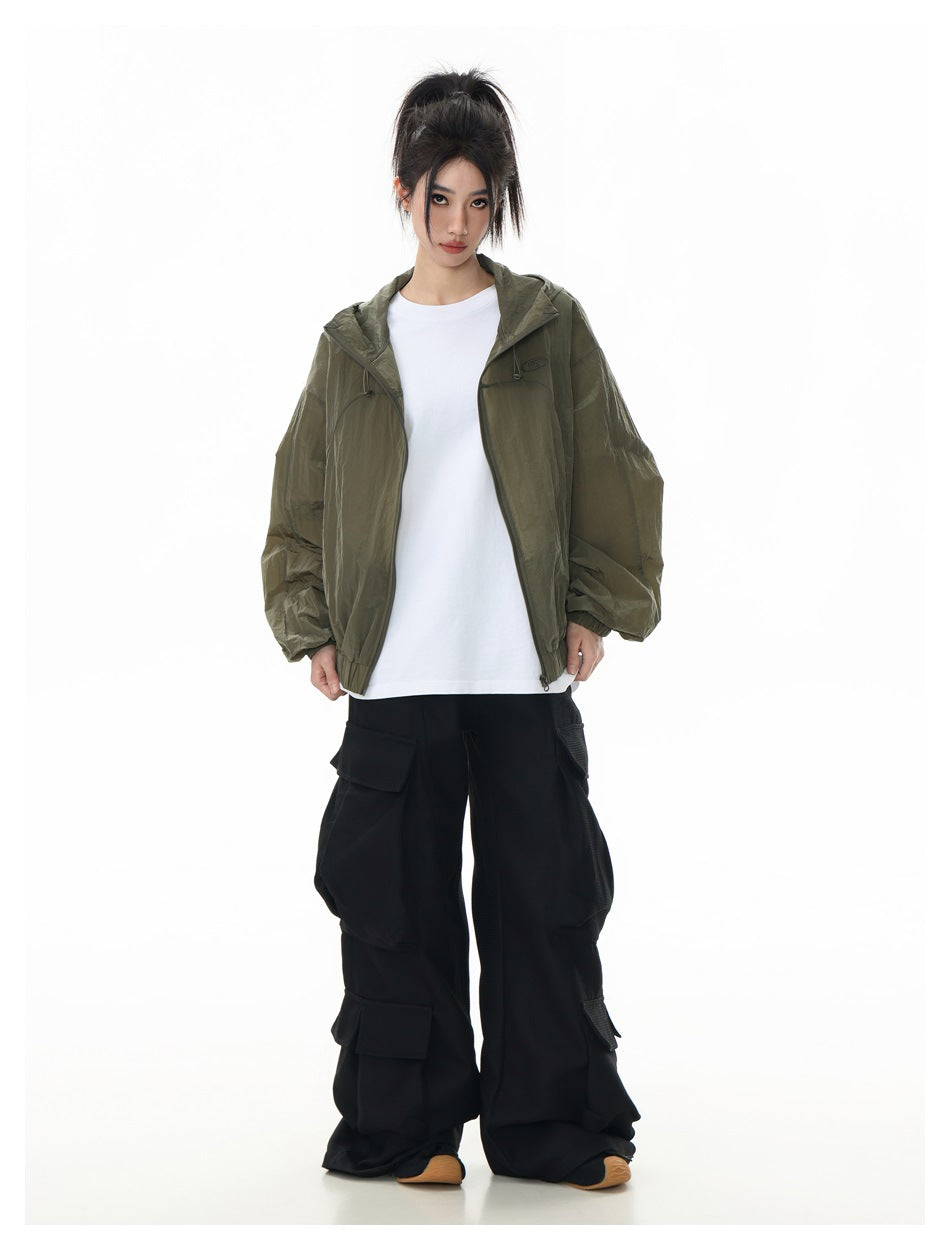 Model wearing an olive hooded zip jacket over a white shirt, with loose black cargo pants; front view.