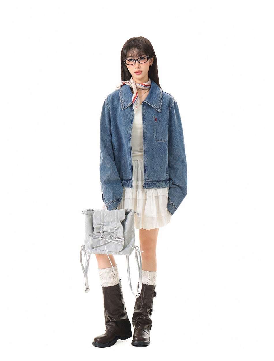 Model wearing blue denim zip jacket over a white top and white tiered skirt with brown boots and a silver bag