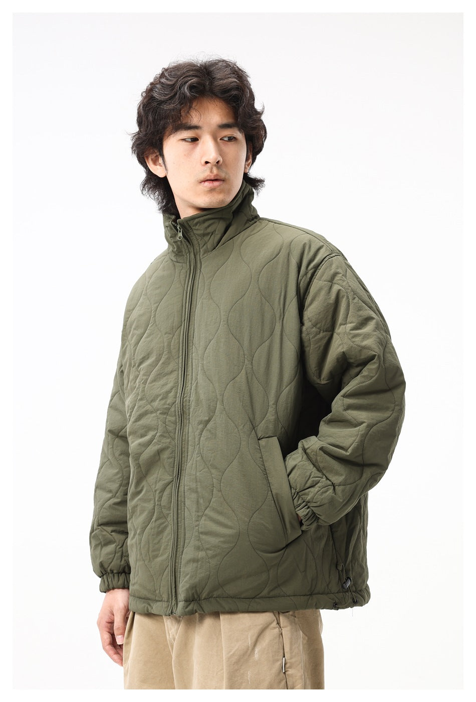 Man wearing an olive quilted jacket with a high collar, front zipper, elastic cuffs and a three-quarter front view.