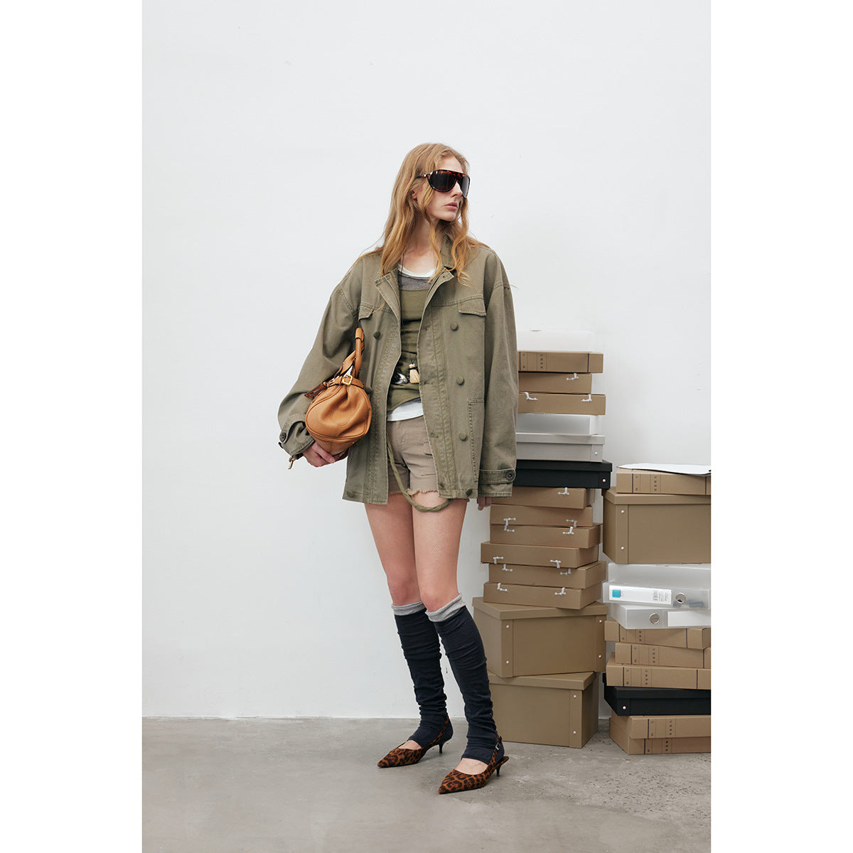 Full-length model wearing an oversized olive utility jacket with chest and lower flap pockets and a button front.