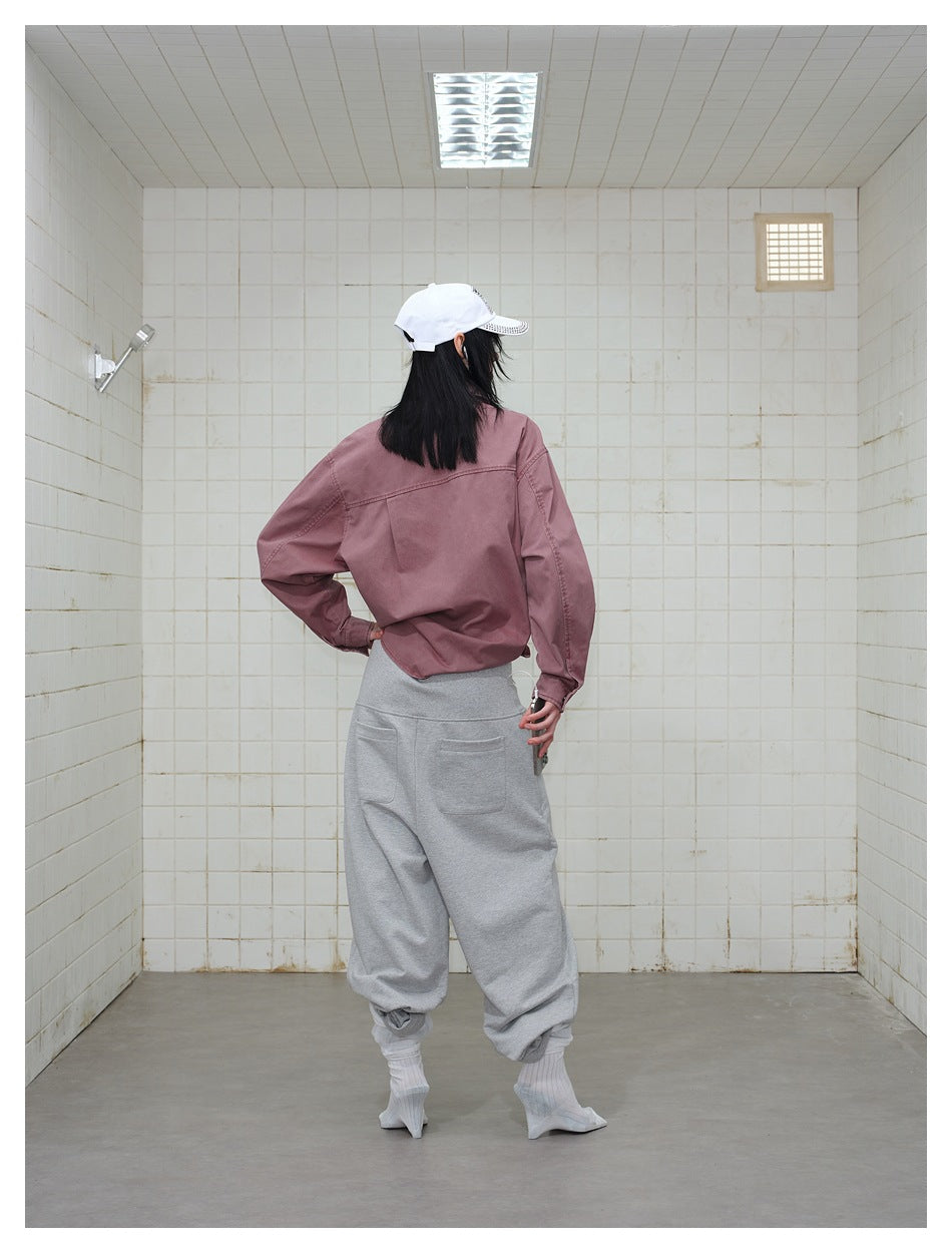 Back view of a model wearing a dusty mauve shirt and loose gray pants with two rear pockets.