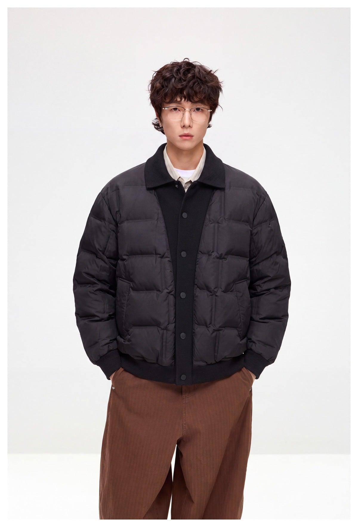 Front view of a model in a dark quilted jacket with a ribbed collar and button placket, paired with brown trousers.