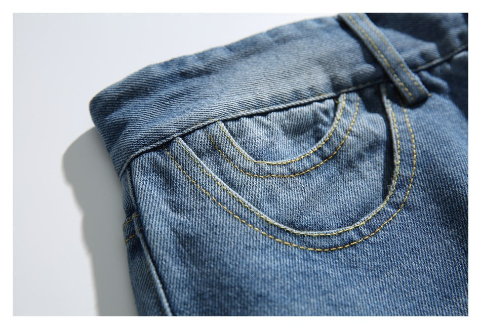 Close-up of a front pocket with curved yellow stitching on faded blue denim.