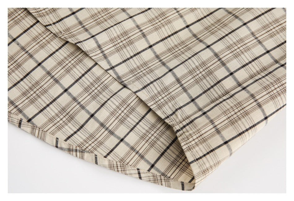 Close-up of the stitched hem and edge of a beige garment with black and brown plaid.