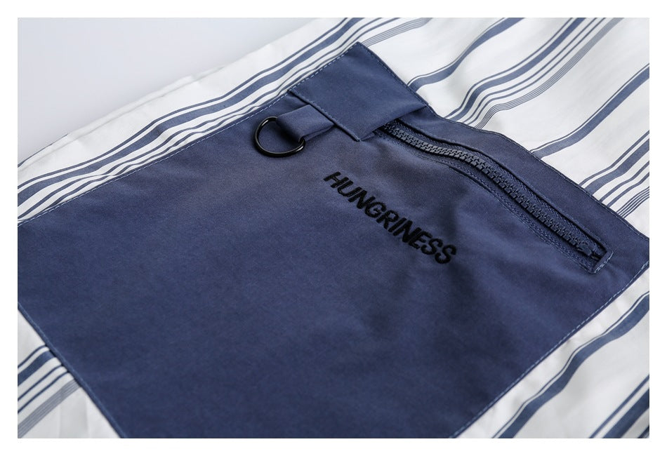 Close-up of the shirt's navy zip pocket, D-ring, and HUNGRINESS embroidery against white navy-striped fabric.