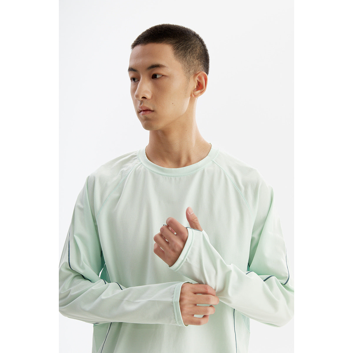 Close view of a model wearing a pale mint long-sleeve crewneck top with dark piping and extended cuffs.