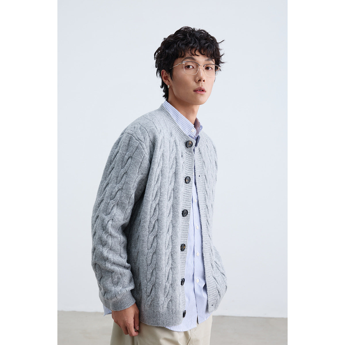 Model wearing a light gray cable-knit button cardigan over a blue-striped shirt.