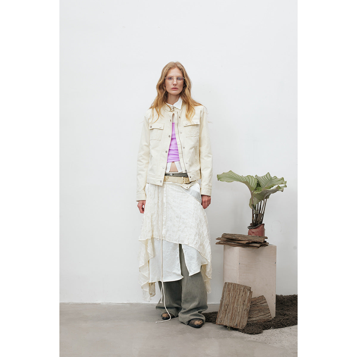 Full-length model wearing an ivory snap-front jacket with flap pockets, layered over a lilac top and white skirt.