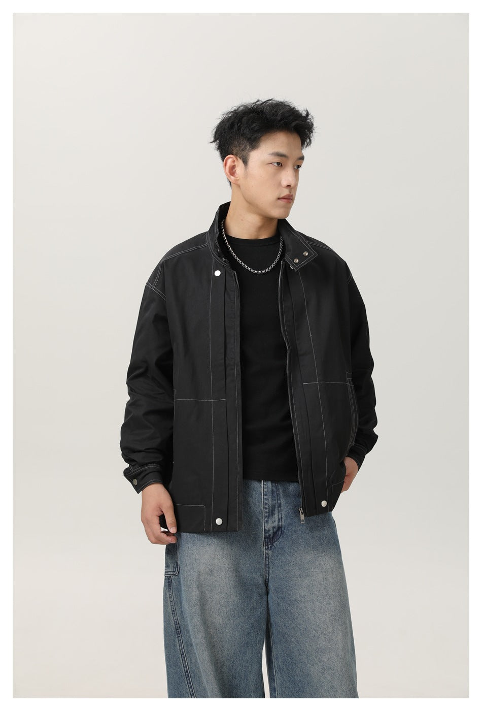 Model wearing an open black jacket with contrast stitching, snap details, and a stand collar.