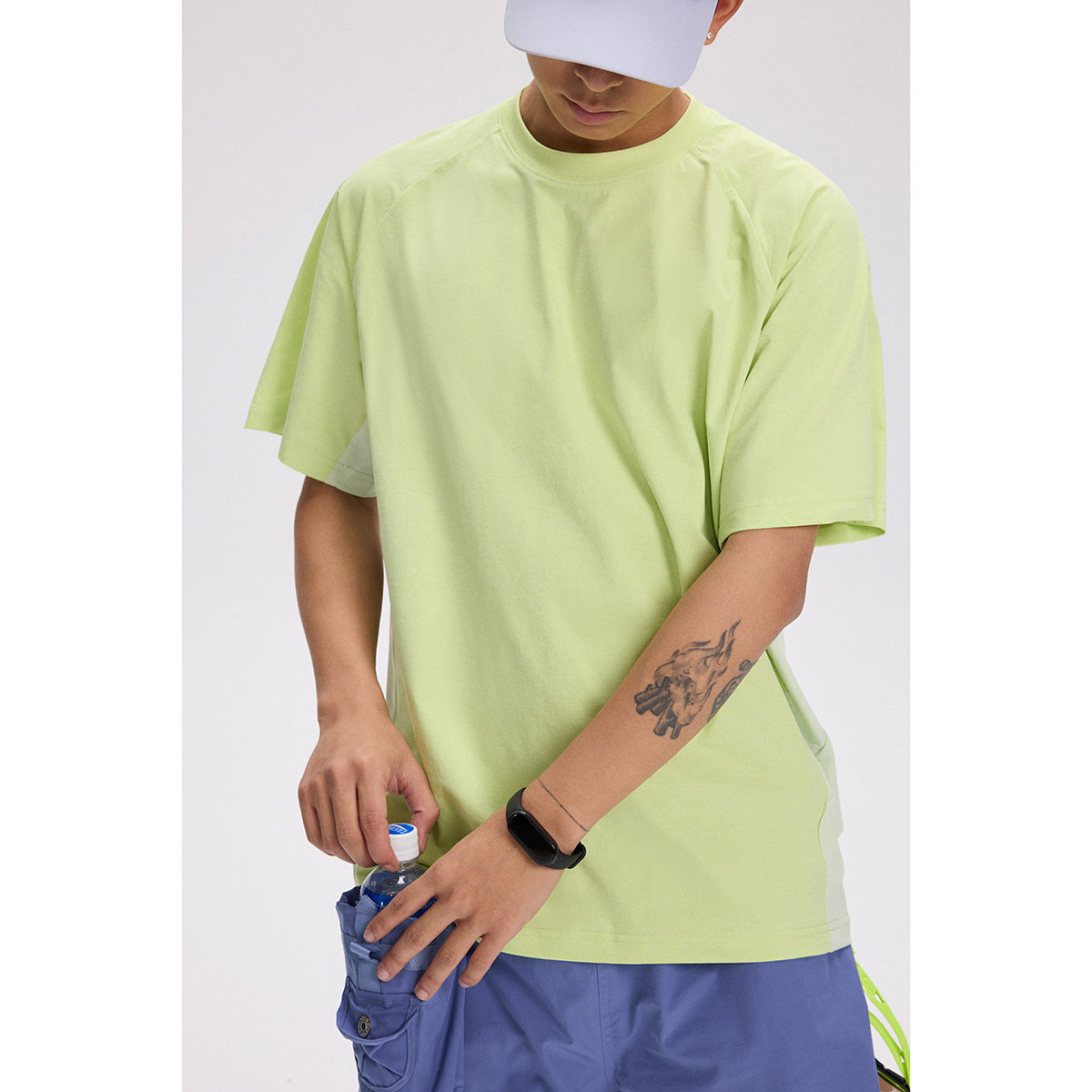 Close view of a model wearing a loose pale lime-green T-shirt and blue shorts.