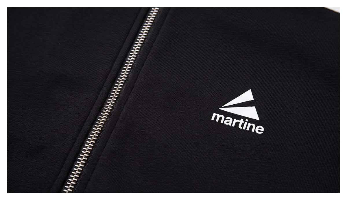 Close-up of a black zip-up jacket with a silver zipper and a white geometric logo with the word “martine.”