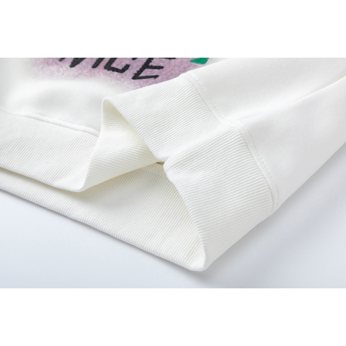 Close-up of the white sweatshirt's ribbed hem and stitching, with part of its colorful print visible.