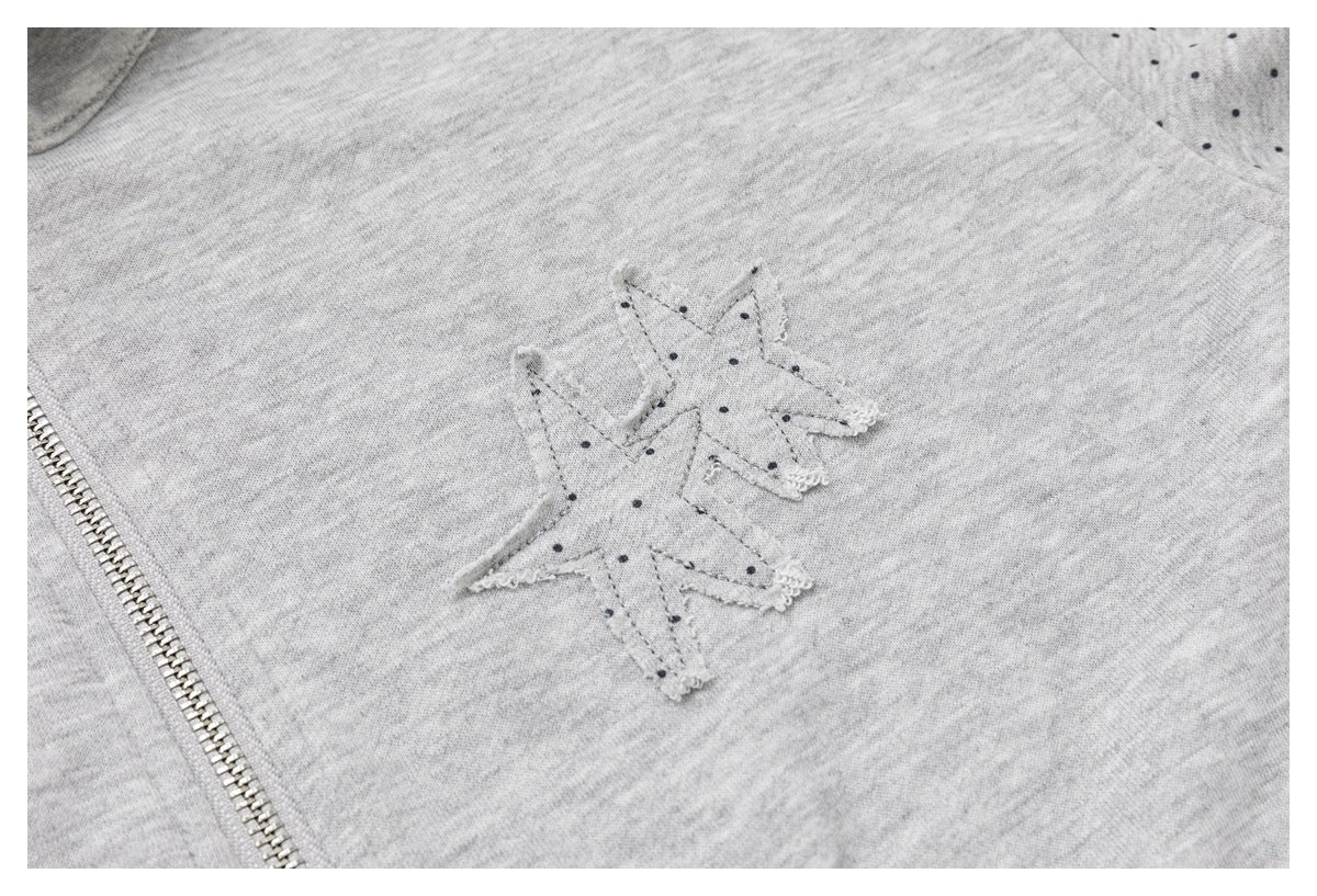 Close-up of a light gray garment with a small dotted star patch and a metal zipper.