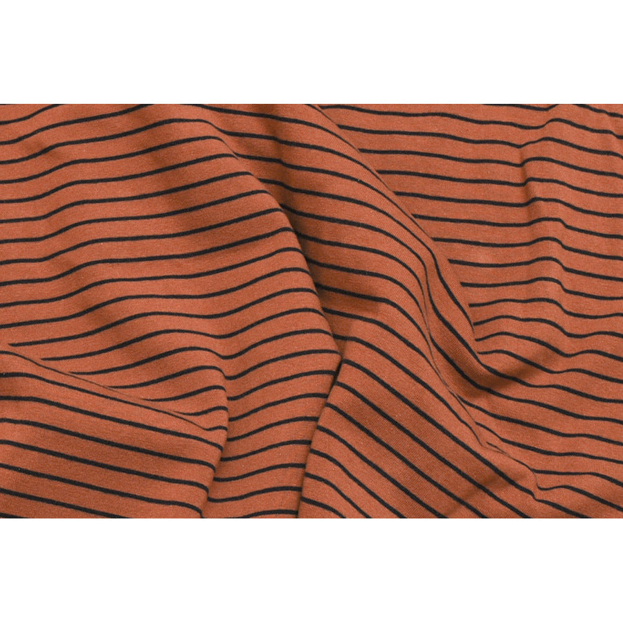 Close-up of softly draped rust-orange fabric with thin black horizontal stripes.